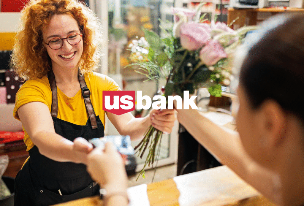 Young red head female florist handing pink roses to a customer and accepting a credit card payment