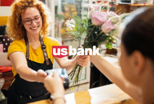 Young red head female florist handing pink roses to a customer and accepting a credit card payment