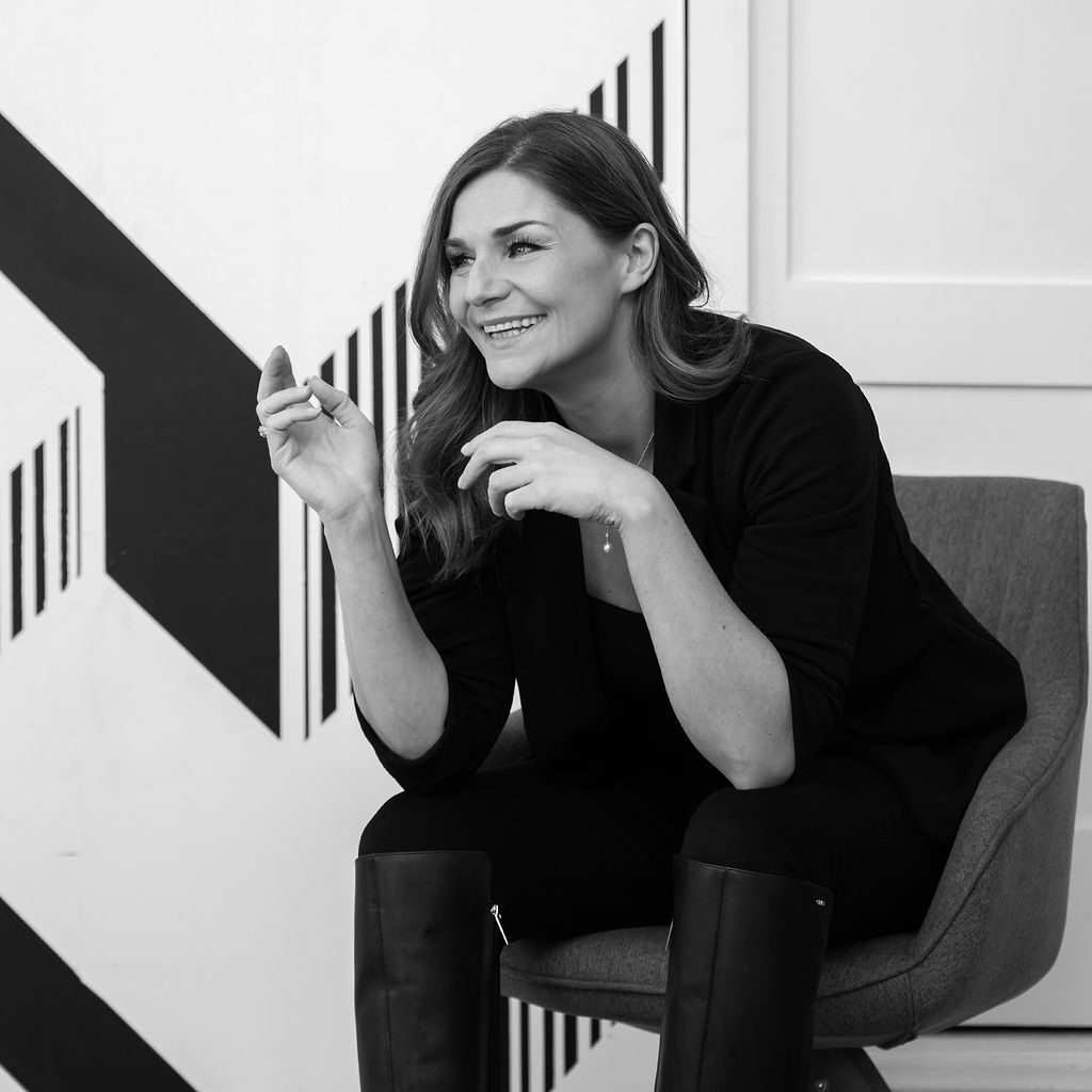 megan derrick looking off camera, smiling, in front of a black and white angular, hatched patterned wall in black and white