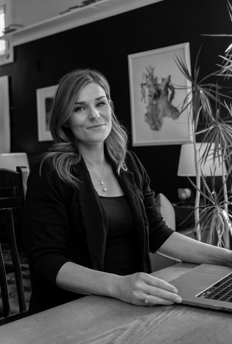 megan derrick working on her laptop at a wooden table in an artistic home studio space